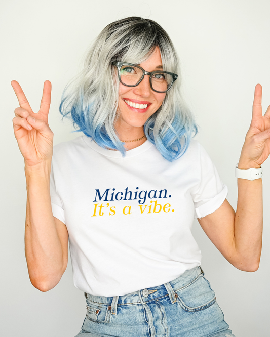Person wearing a white t-shirt with 'Michigan. It's a vibe.' text, making peace signs.